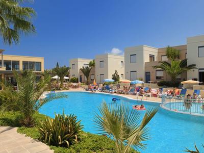 Großer blauer Pool vor modernen weißen Gebäuden mit Palmen und Menschen bei sonnigem Wetter.