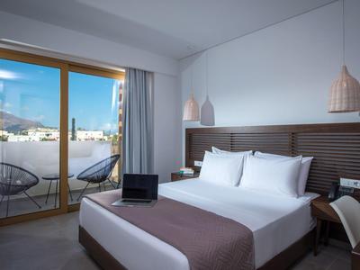 Modern hotelkamer met tweepersoonsbed, laptop op het bed en balkon met uitzicht op zee.