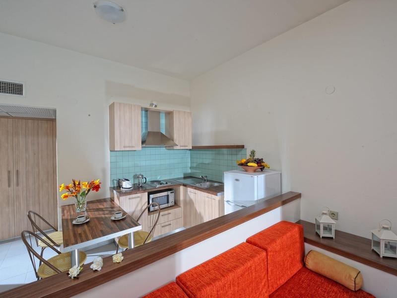 Moderne kleine keuken met glazen achterwand, eettafel en oranje bank in een compacte woonruimte.