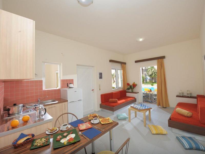 Kleine moderne vakantiewoning met kitchenette, eettafel en twee rode banken.