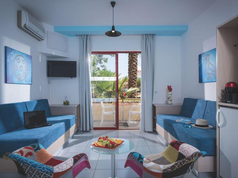 Moderne woonkamer met blauwe banken, kleurrijke stoelen en uitzicht op een terras met palmbomen.