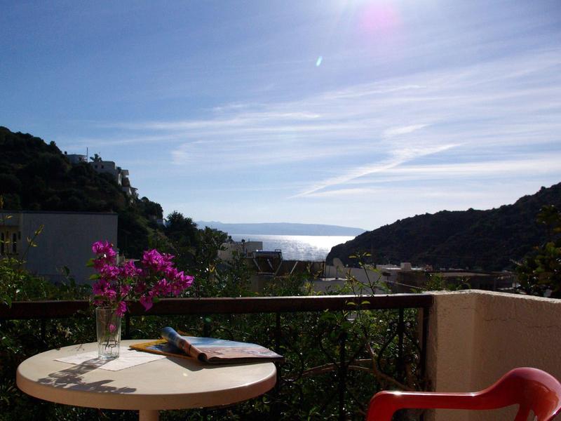 Terrasse mit einem Tisch, einem roten Stuhl und Blick auf das Meer zwischen Hügeln.