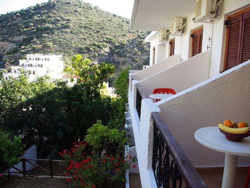 Balkon mit Tisch und Obstschale, Blick auf Hügel und Gebäude bei Sonnenschein.