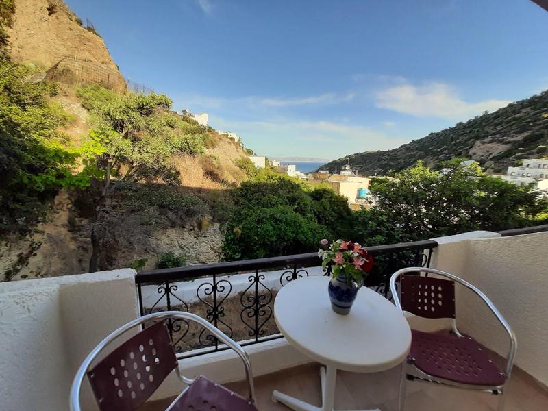 Balkon mit Tisch, Stühlen und Blumen mit Blick auf Hügel und Meer im Hintergrund.