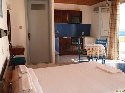 Ein helles Zimmer mit Bett, kleinem Esstisch, Fenster mit Gardinen und Blick nach draußen.