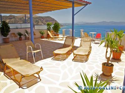 Terrasse mit Sonnenliegen, Pflanzen und Blick auf ruhiges blaues Meer und Berge am Horizont.