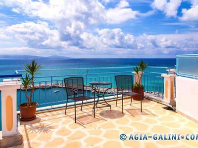 Balkon mit Tisch, Stühlen und Pflanzen, Blick auf das blaue Meer und bewölkten Himmel.