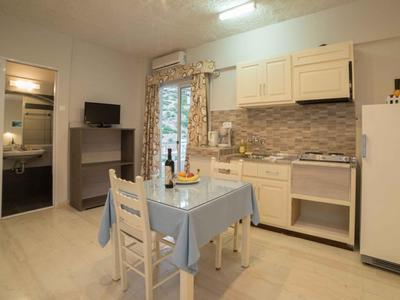 Kleine Küche mit Esstisch, zwei Stühlen, Kühlschrank und Zugang zu Bad und Garten