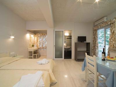 Helles Hotelzimmer mit weißem Mobiliar, zwei Betten, Tisch und kleinem Fernseher.