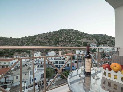 Balkon mit Glasplatte, Weinflasche, Obstkorb und Blick auf Hügel und Stadt.