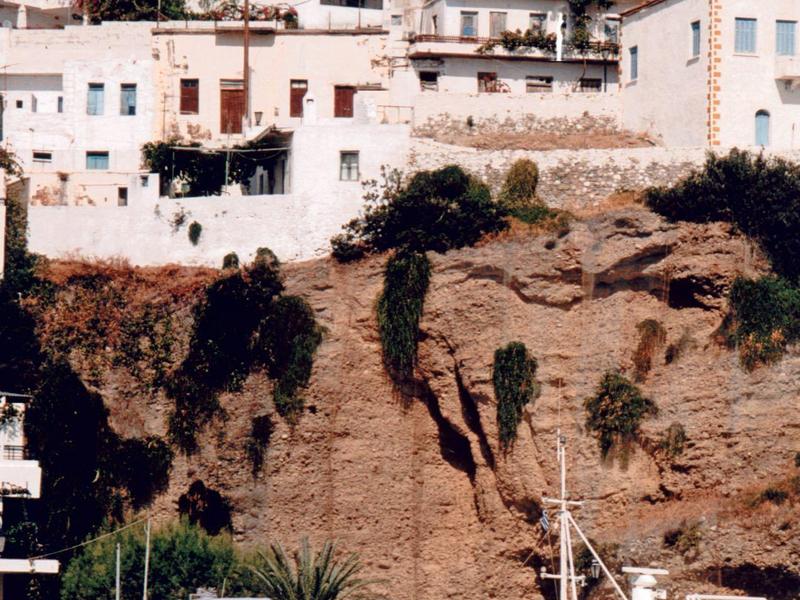 Boote liegen im Hafen vor Klippen mit weißen Gebäuden und blauem Himmel.