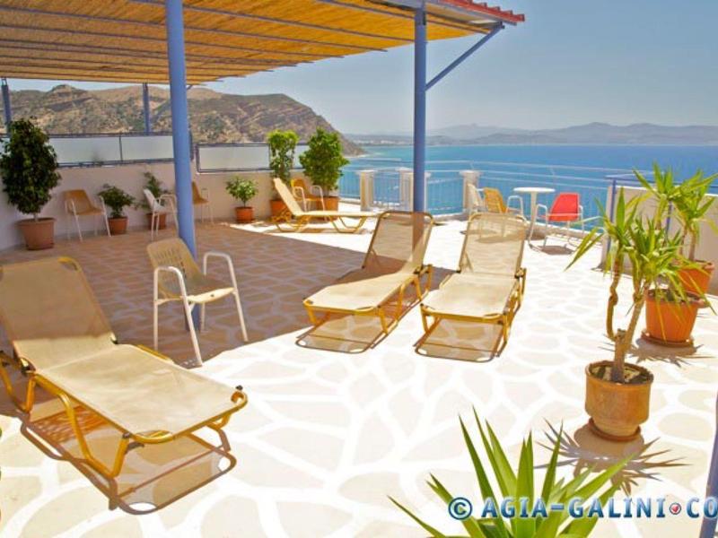 Helle Terrasse mit Liegestühlen, Pflanzen und Meerblick unter blauer Sonne.
