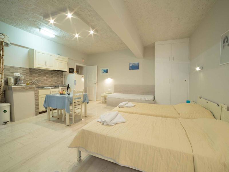 Ein einfaches Hotelzimmer mit zwei Betten, einem Tisch, Stühlen und einer kleinen Küchenzeile.