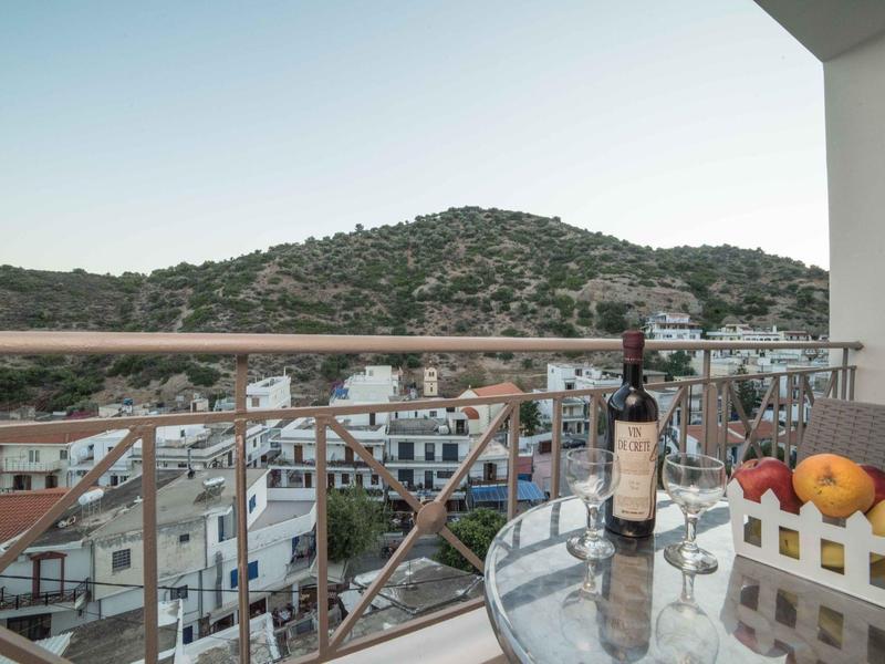 Balkon mit Glasplatte, Weinflasche, Obstkorb und Blick auf Hügel und Stadt.