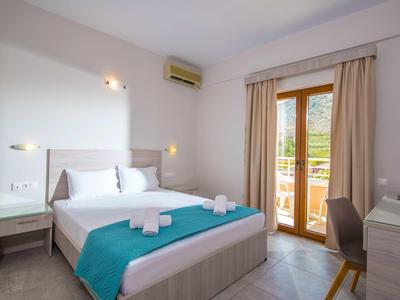 Camera d'hotel luminosa con letto matrimoniale, copriletto turchese e terrazza con vista sul verde.