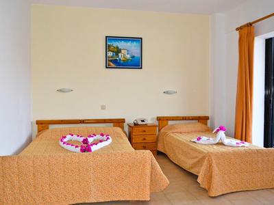 Camera d'hotel con due letti, un comodino e una finestra con tende arancioni.