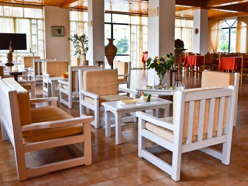 Zona pranzo luminosa dell'hotel con mobili bianchi in legno e grandi finestre.