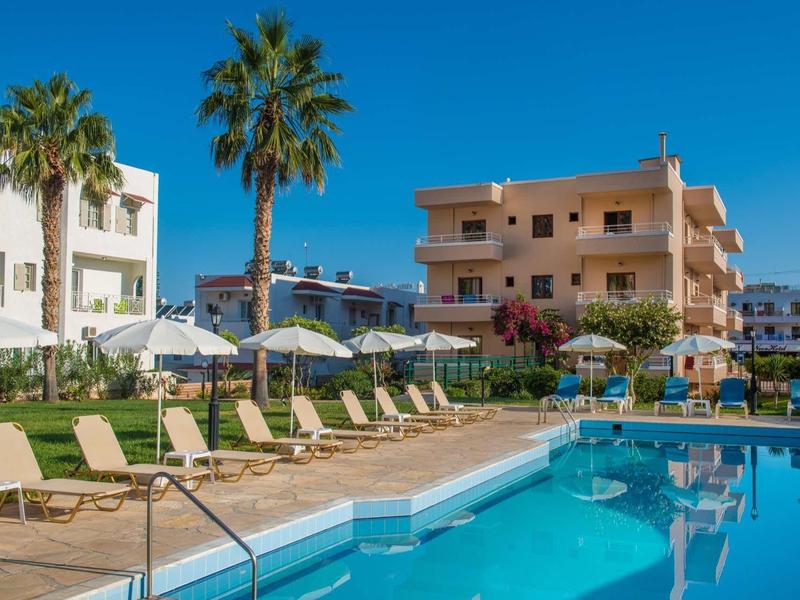 Area ricreativa con piscina, lettini e ombrelloni davanti a edifici alberghieri sotto un cielo limpido.