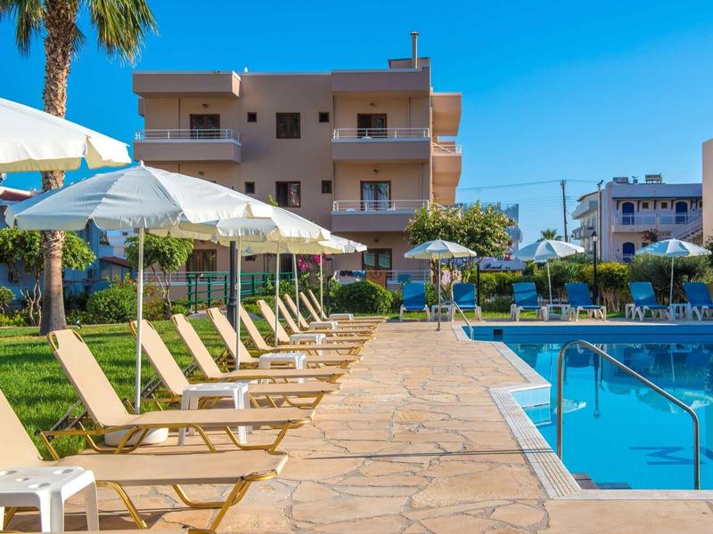 Area piscina con lettini e ombrelloni davanti a un edificio alberghiero in una giornata soleggiata.