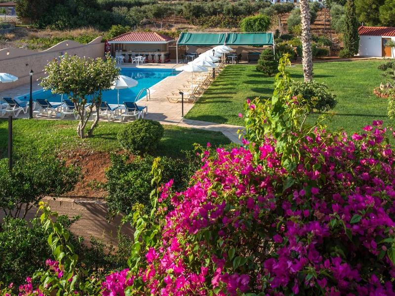 Giardino verde con fiori rosa, piscina e area salotto in un resort.