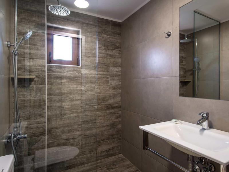 Bagno moderno con ampia doccia a pioggia, lavabo e piastrelle marrone chiaro.