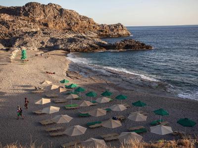 Strand mit bunten Sonnenschirmen, felsiger Küste und ruhigem Meer bei klarem Himmel.