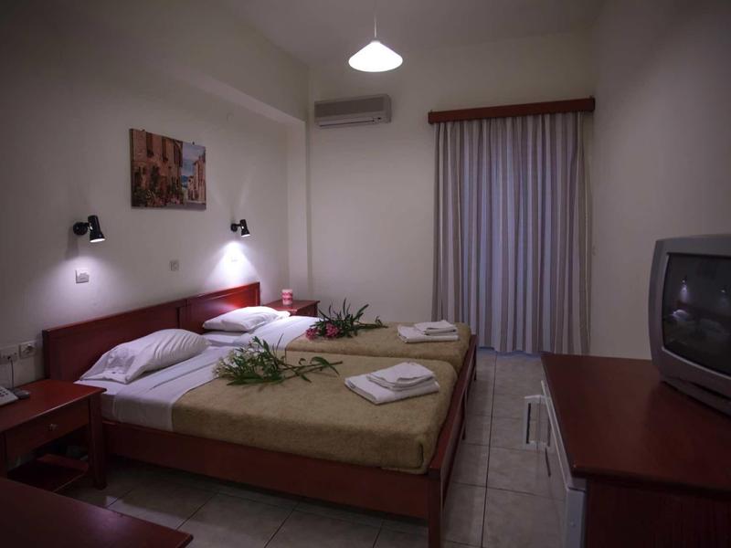 Kleines Schlafzimmer mit zwei Einzelbetten, Nachttischen, TV, Klimaanlage und Vorhang an der Tür.