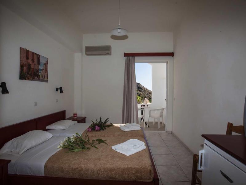 Einfaches Hotelzimmer mit Doppelbett, Klimaanlage, kleinem Balkon und TV auf Kommode.