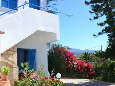 Casa vacanza bianca con finestre blu e giardino fiorito sotto cielo terso.