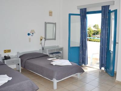 Camera d'hotel luminosa con due letti singoli, cornice della porta blu e vista sulla piscina.