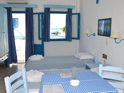 Stanza luminosa con letti, tavolo a quadri blu e vista sul mare.