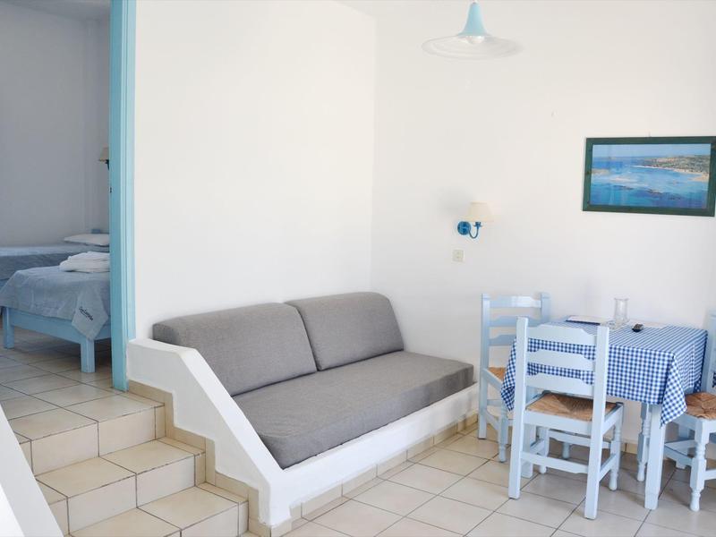 Zona giorno luminosa con divano grigio e piccolo tavolo da pranzo accanto a una camera da letto.