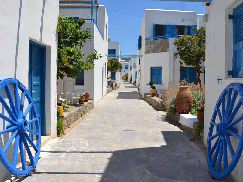 Sentiero stretto con edifici imbiancati e finestre e porte blu, decorato con ruote di carro blu.