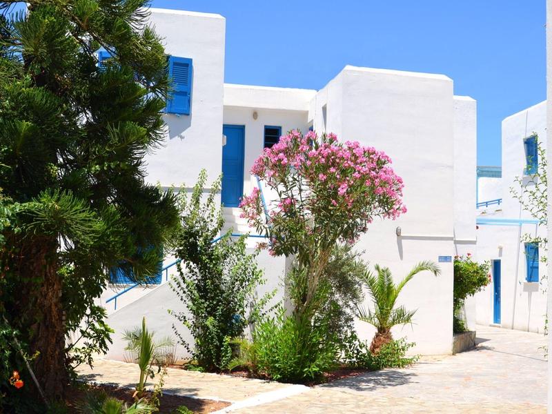 Edificio bianco con fiori colorati e piante verdi in una giornata di sole.