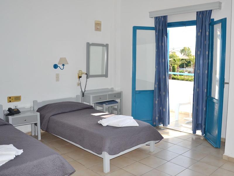 Camera d'hotel luminosa con due letti singoli, cornice della porta blu e vista sulla piscina.