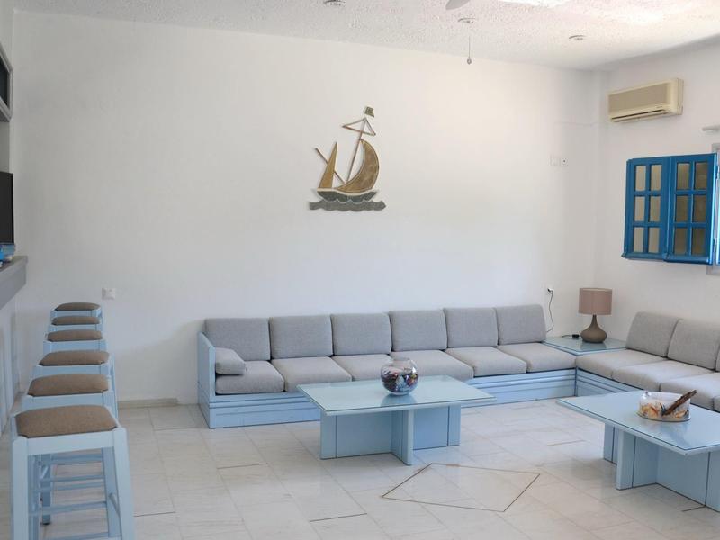 Zona giorno moderna con divano angolare grigio, sgabelli, tavolo blu e finestra con cornice blu.