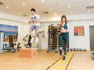 Twee mensen trainen in een lichte fitnessruimte met een springdoos en een coördinatieladder.