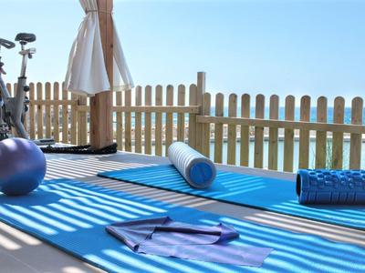 Yoga mat met fitnessaccessoires op terras met uitzicht op zee en houten hek.