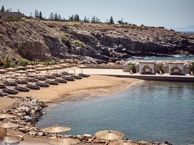 Leeg strand met parasols, ligstoelen en kleine cabana's bij rotskust en kalm water.