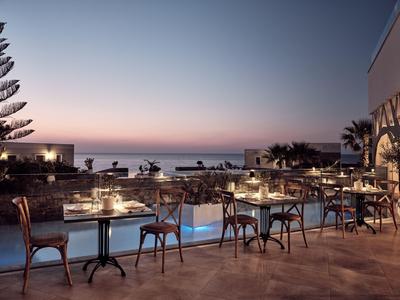 Hotelterras in de avond met verlichte tafels en uitzicht op zee bij zonsondergang.