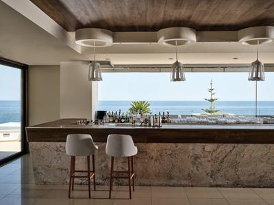 Moderner Barbereich mit Marmorfront, weißen Barhockern und Meerblick durch große Fenster.