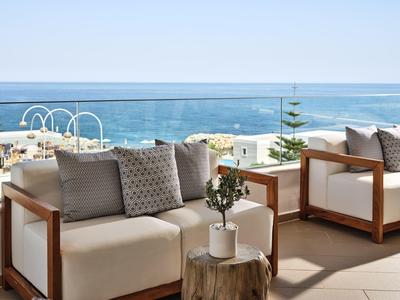Terrasse mit bequemen weißen Sesseln, Kissen und kleinem Tisch vor klarem Meerblick.