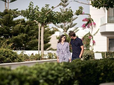 Ein Paar geht auf einem Gehweg, umgeben von grünen Bäumen und Sträuchern, bei Tageslicht.