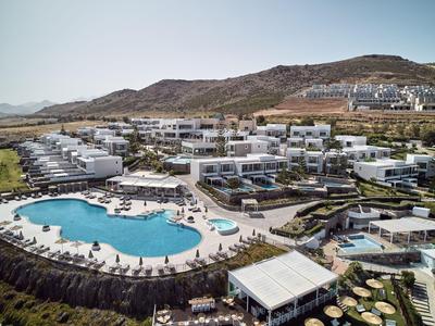 Modern resort met groot zwembad en witte gebouwen voor heuvels onder een heldere lucht.