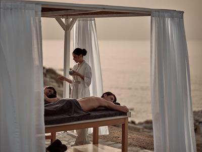 Eine entspannte Massage am Strand bei Sonnenuntergang mit sanften weißen Vorhängen.