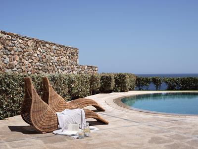 Rundlicher Pool mit Terrakotta-Liegen und grünen Hecken unter klarem blauem Himmel.