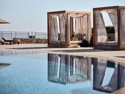 Zwembad met twee cabana's en uitzicht op zee op een zonnige dag.