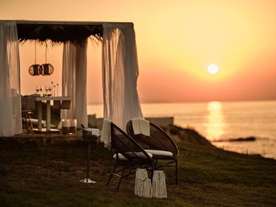 Zwei Stühle vor einer überdachten Lounge am Meer bei Sonnenuntergang mit goldgelbem Himmel.