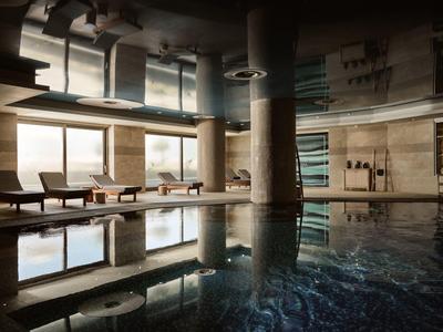 Innenraum mit großem Pool, Säulen, Sitzbereich und Panoramafenstern, warme Beleuchtung.