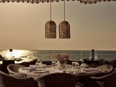 Elegante gedekte tafel met rieten stoelen aan zee bij zonsondergang.